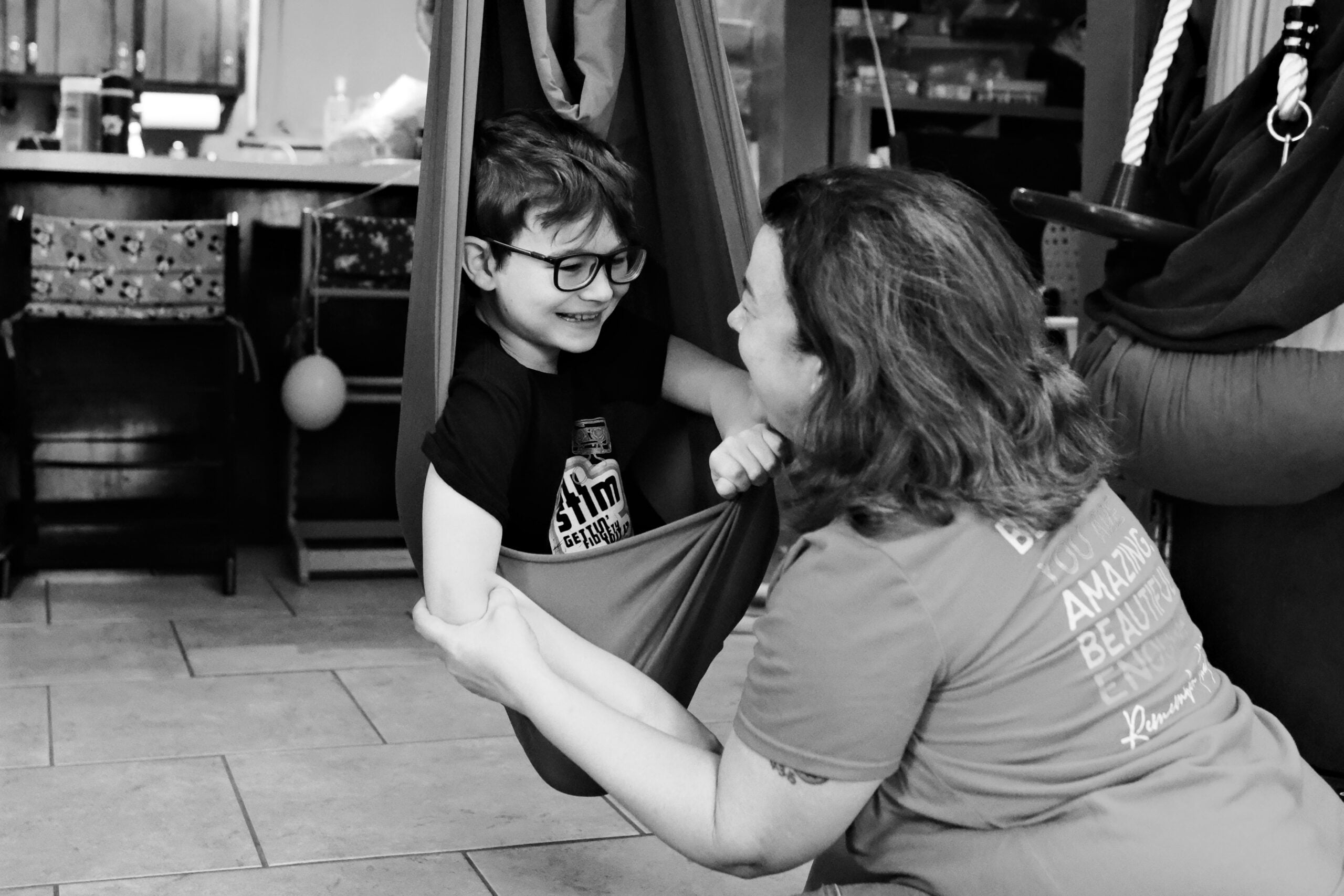 Mother smiling with her son as he sits in an indoor sensory swing