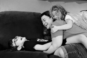 Mother laughing as her daughter hugs her from behind and her son lies beside her
