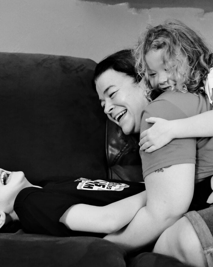 Mother laughing as her daughter hugs her from behind and her son lies beside her